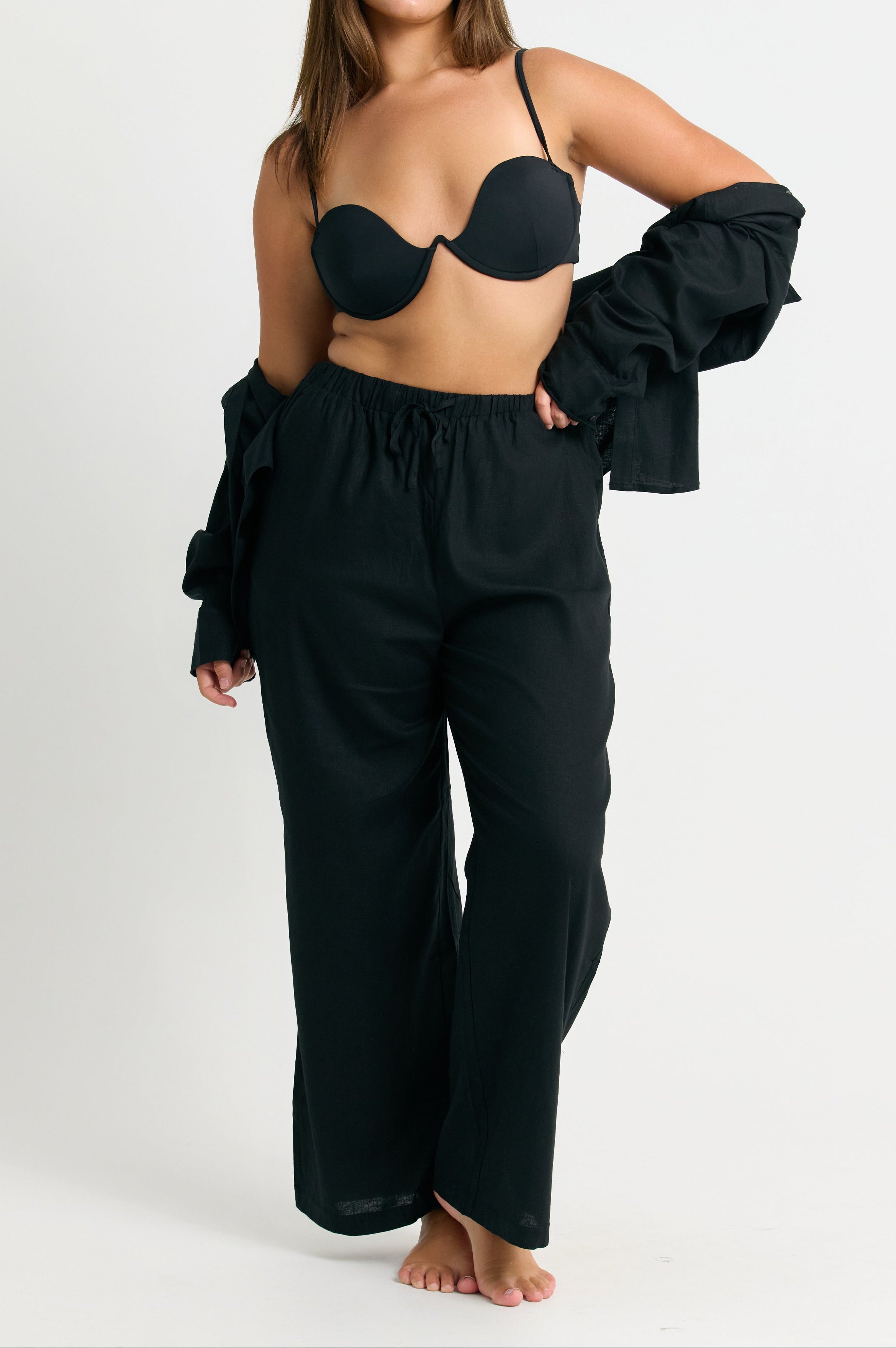 Woman wearing a black bikini top and wide-leg linen pants on a white background