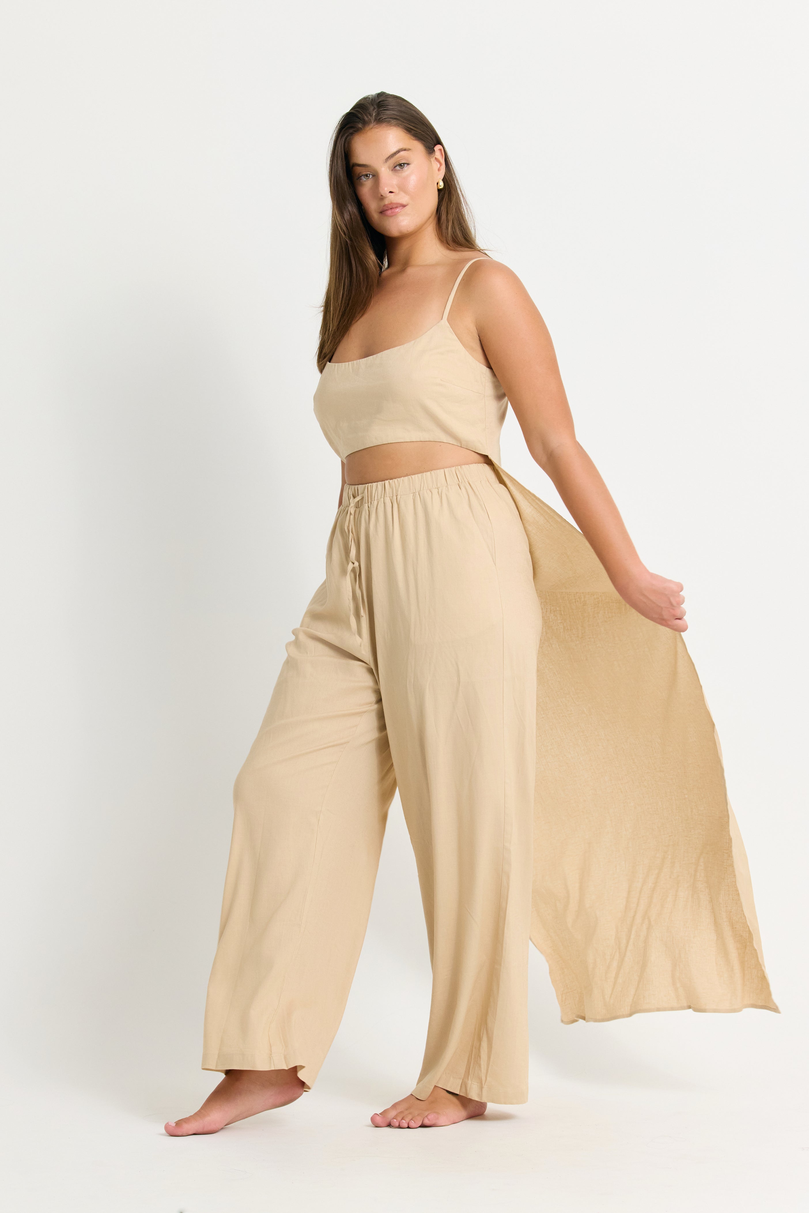 Woman wearing a beige outfit with wide-leg pants and a crop top with a back train on a white background