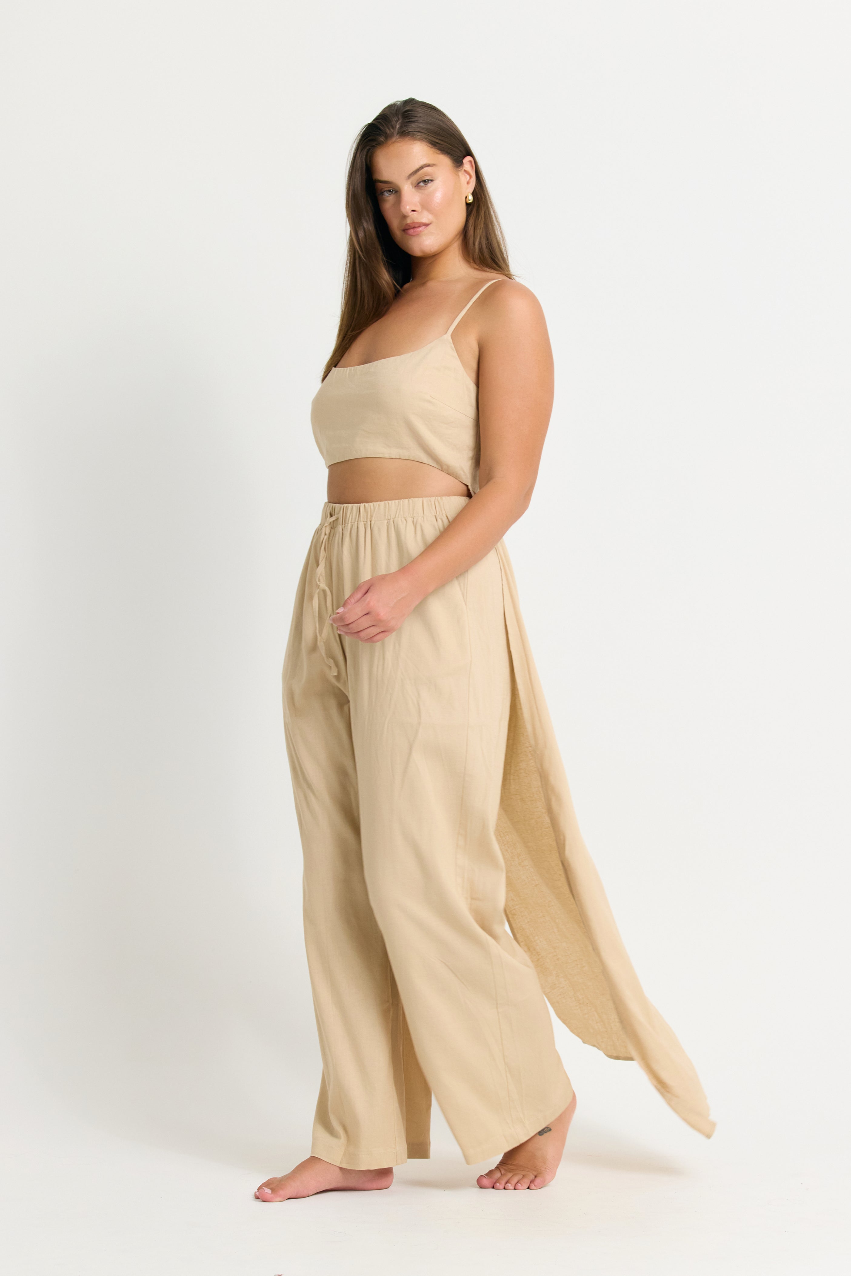 Woman wearing a beige crop top with train with and wide leg pants  with a white background 
