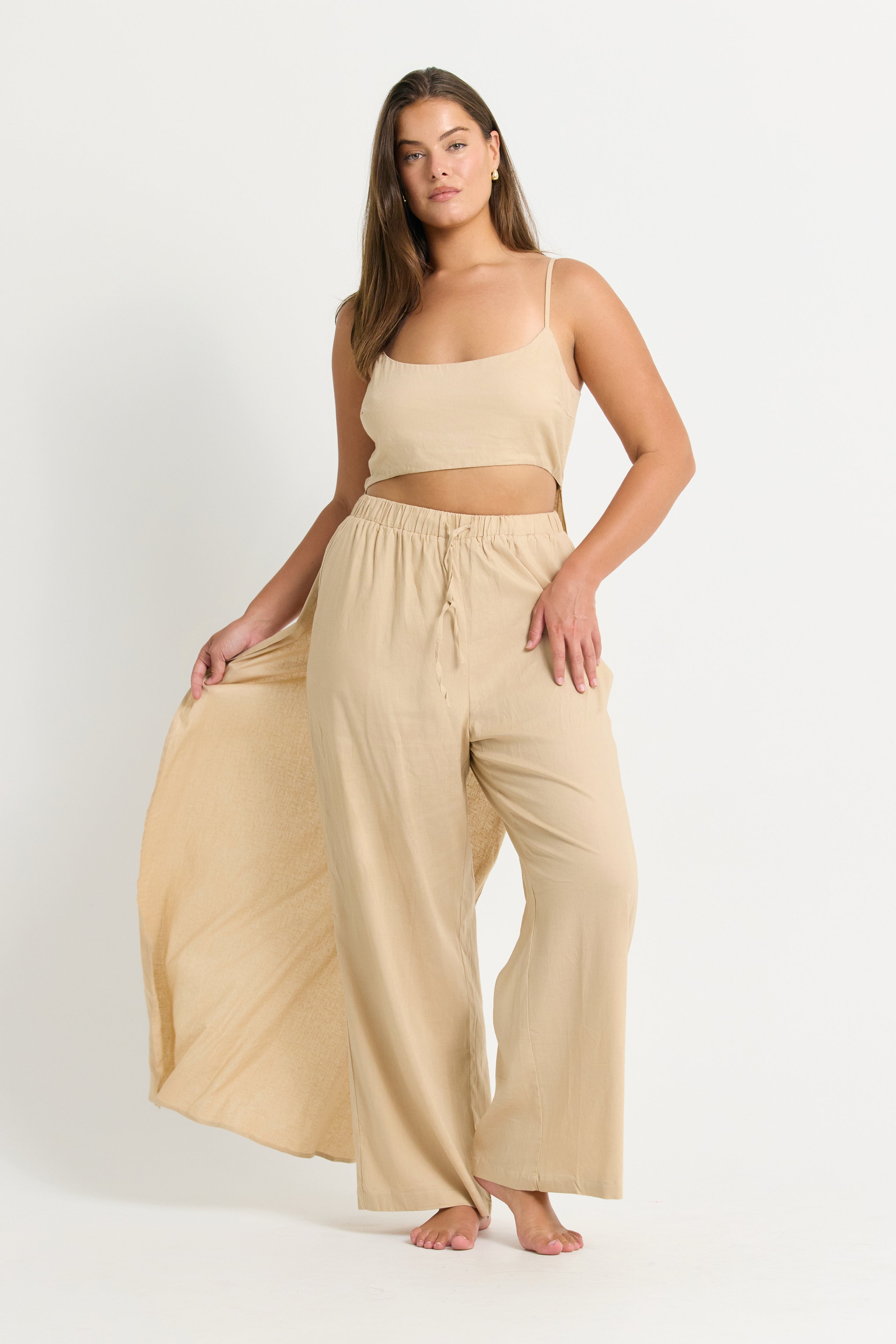 Woman wearing a beige top with train and wide-leg pants on a white background