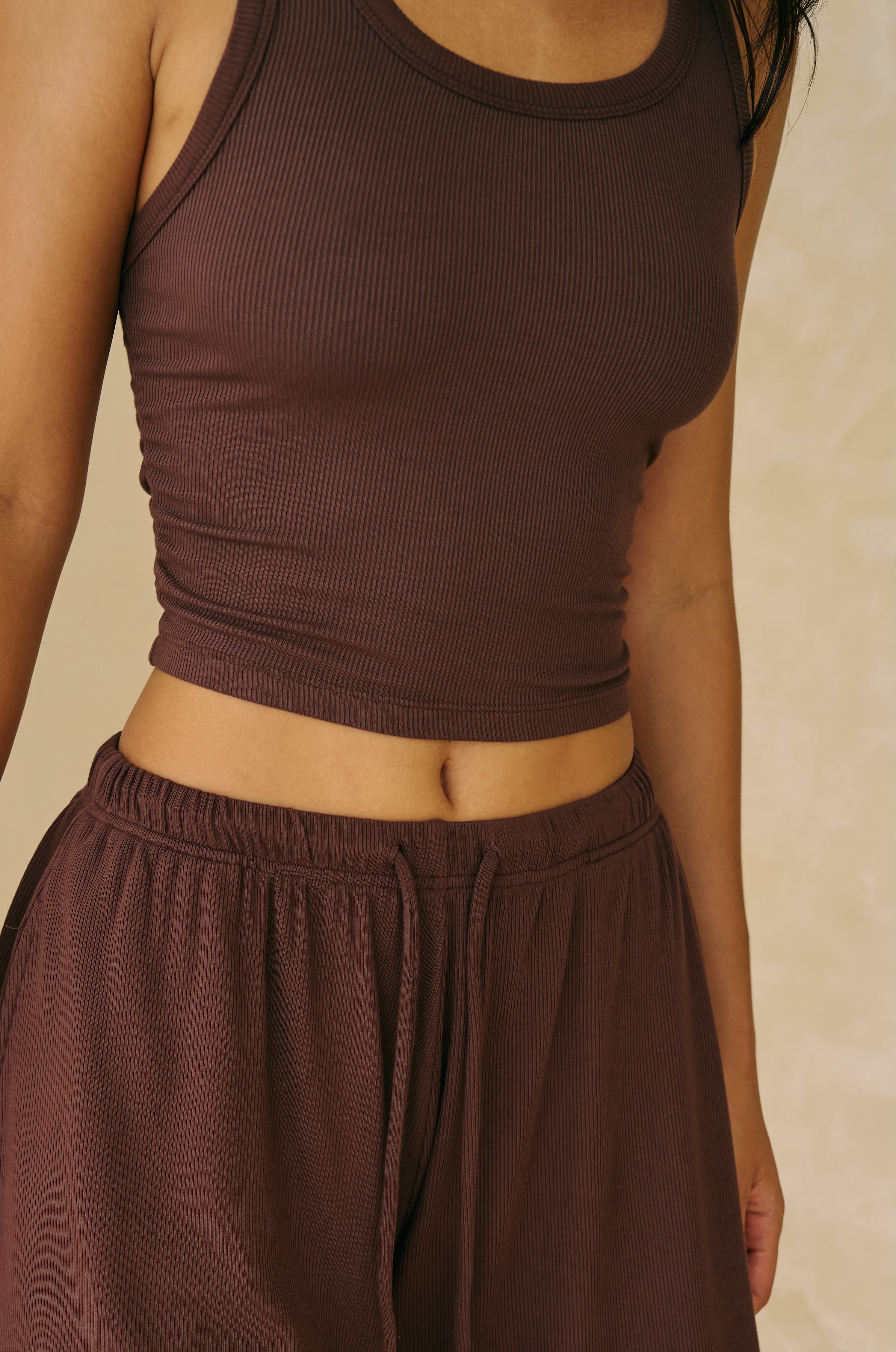 WOMAN WEARING CHOCOLATE BROWN TANK AND SHORTS ON CREAM WALL