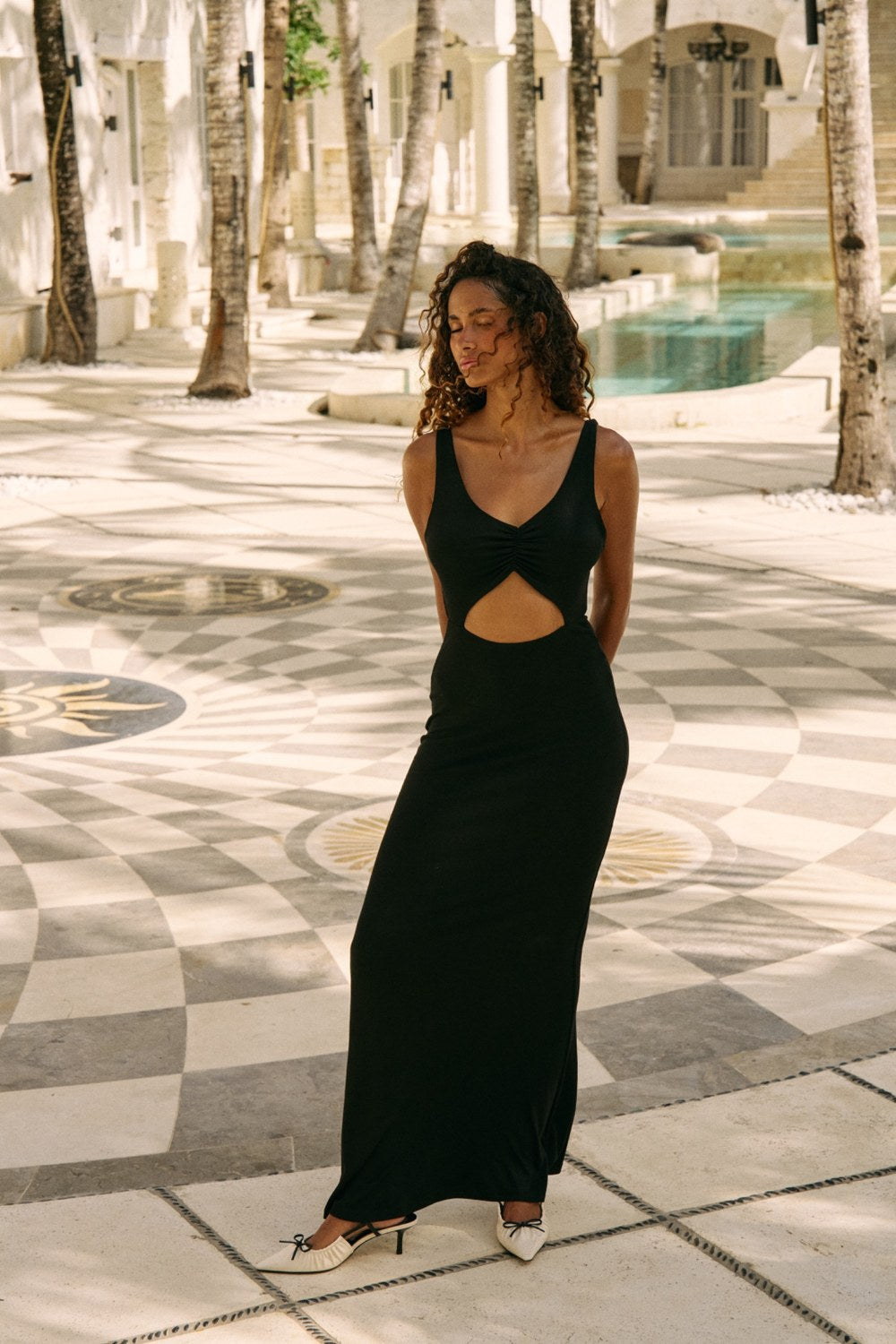 Woman in a black dress with cutouts standing on a patterned pavement with palm trees in the background