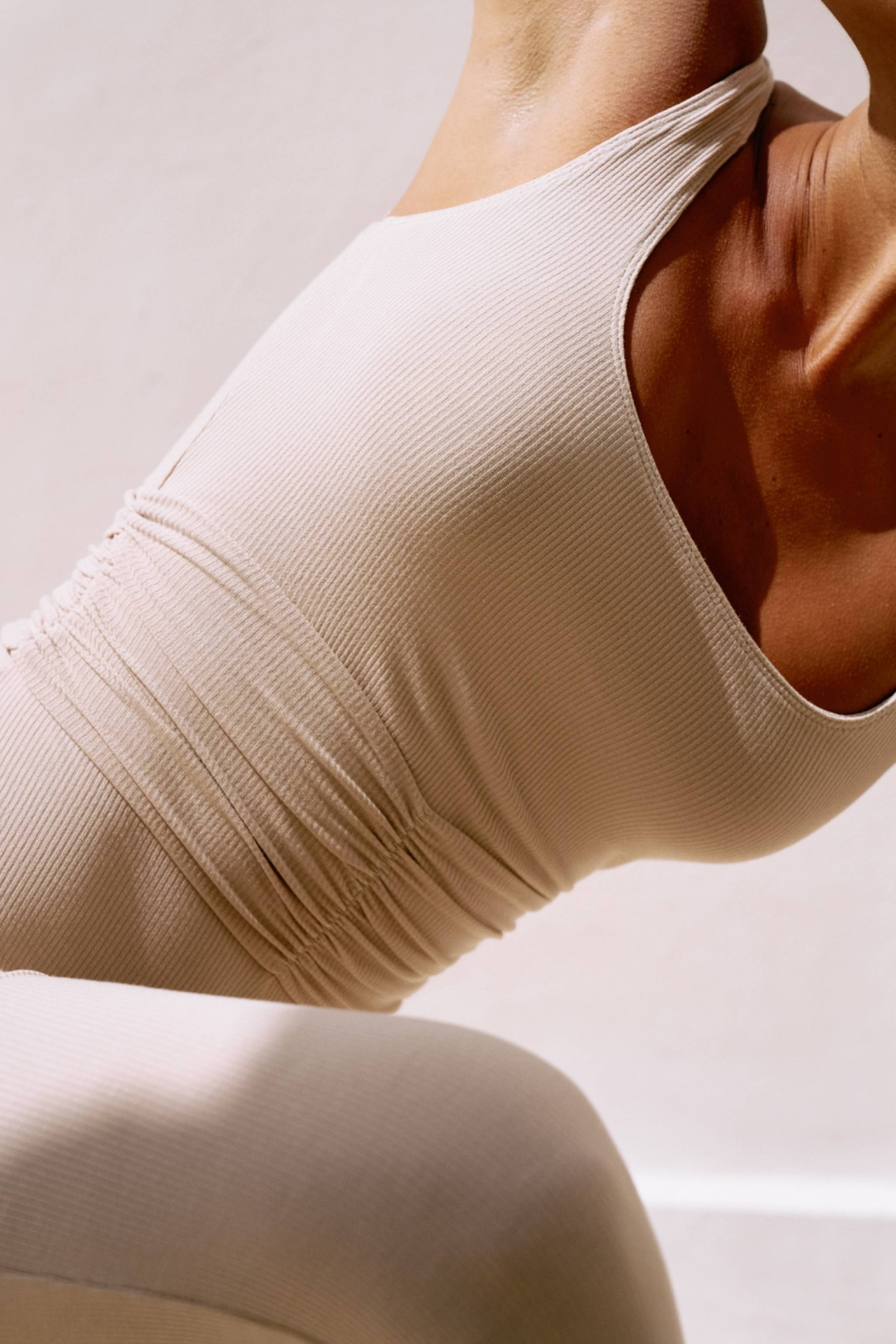 Close-up of a person wearing a beige/coconut sleeveless romper against a neutral background