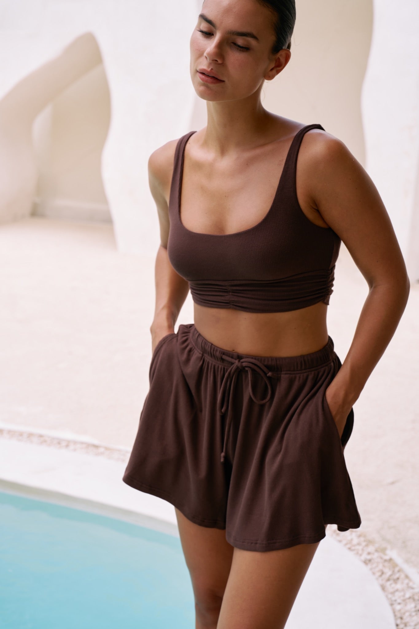 Woman standing by pool wearing the Demi Top with Simi Bottom shorts in Chocolate ribbed knit