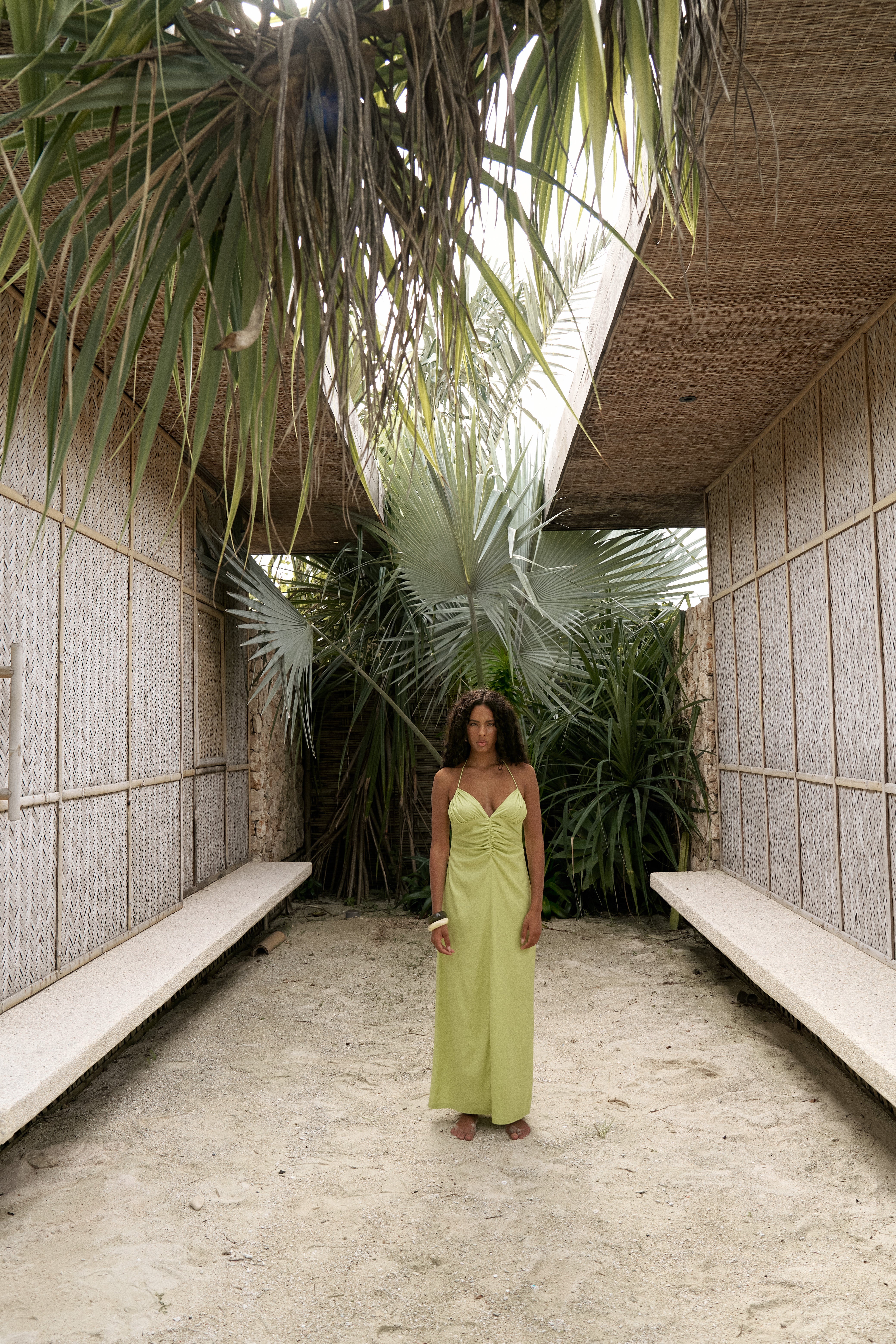 Woman in a green dress standing in a modern architectural setting with plants and benches.