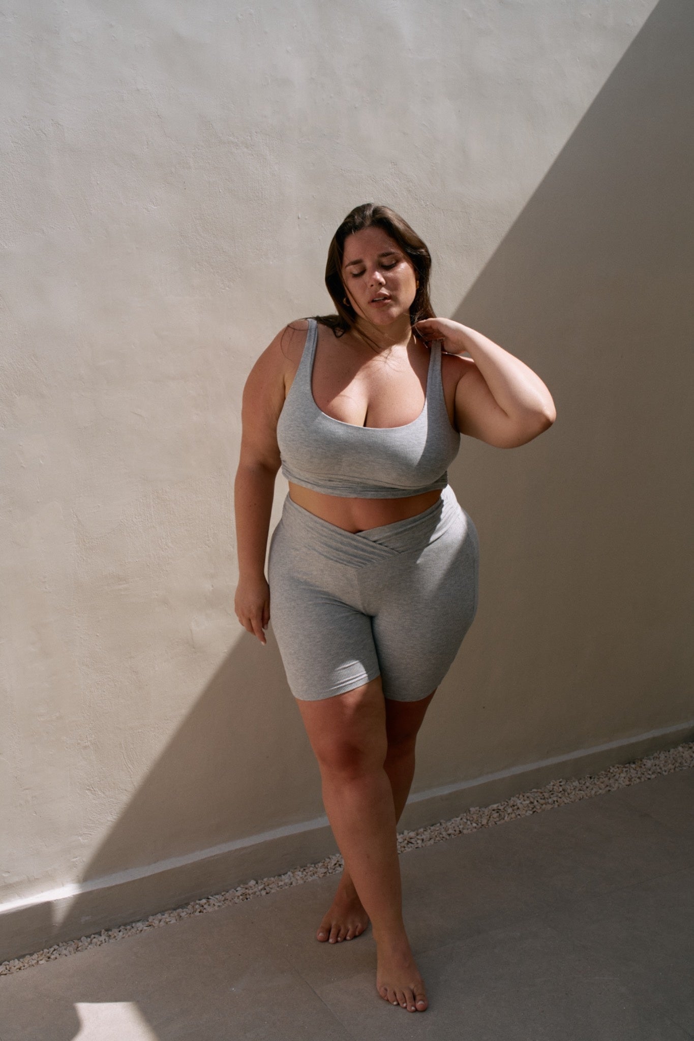 Close-up of a woman wearing the Demi Top and Demi Bottom in Misty. The ribbed grey scoop-neck top and crossover waistband bike shorts are shown in detail