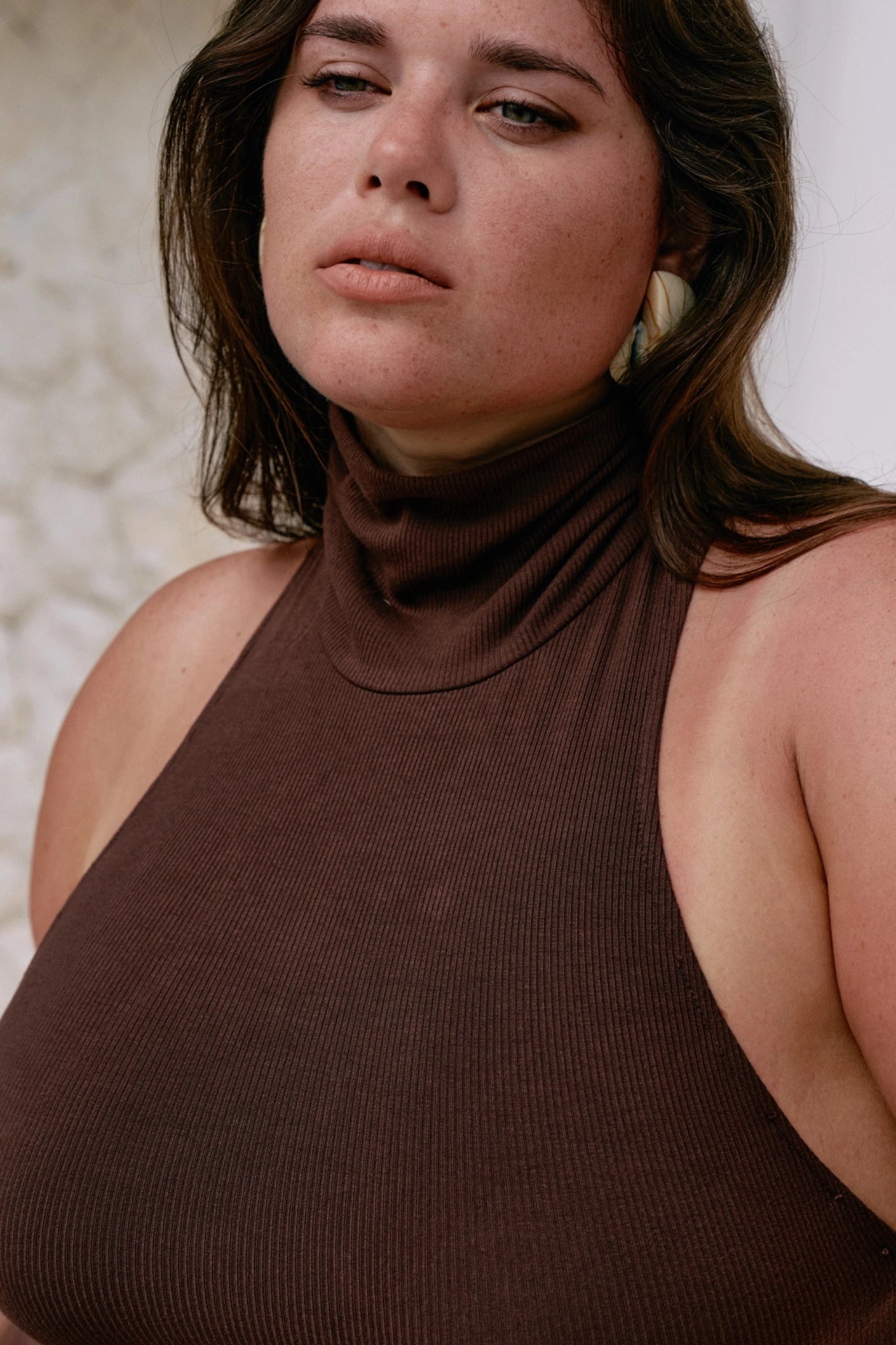 Woman wearing a brown sleeveless turtleneck dress against a neutral background
