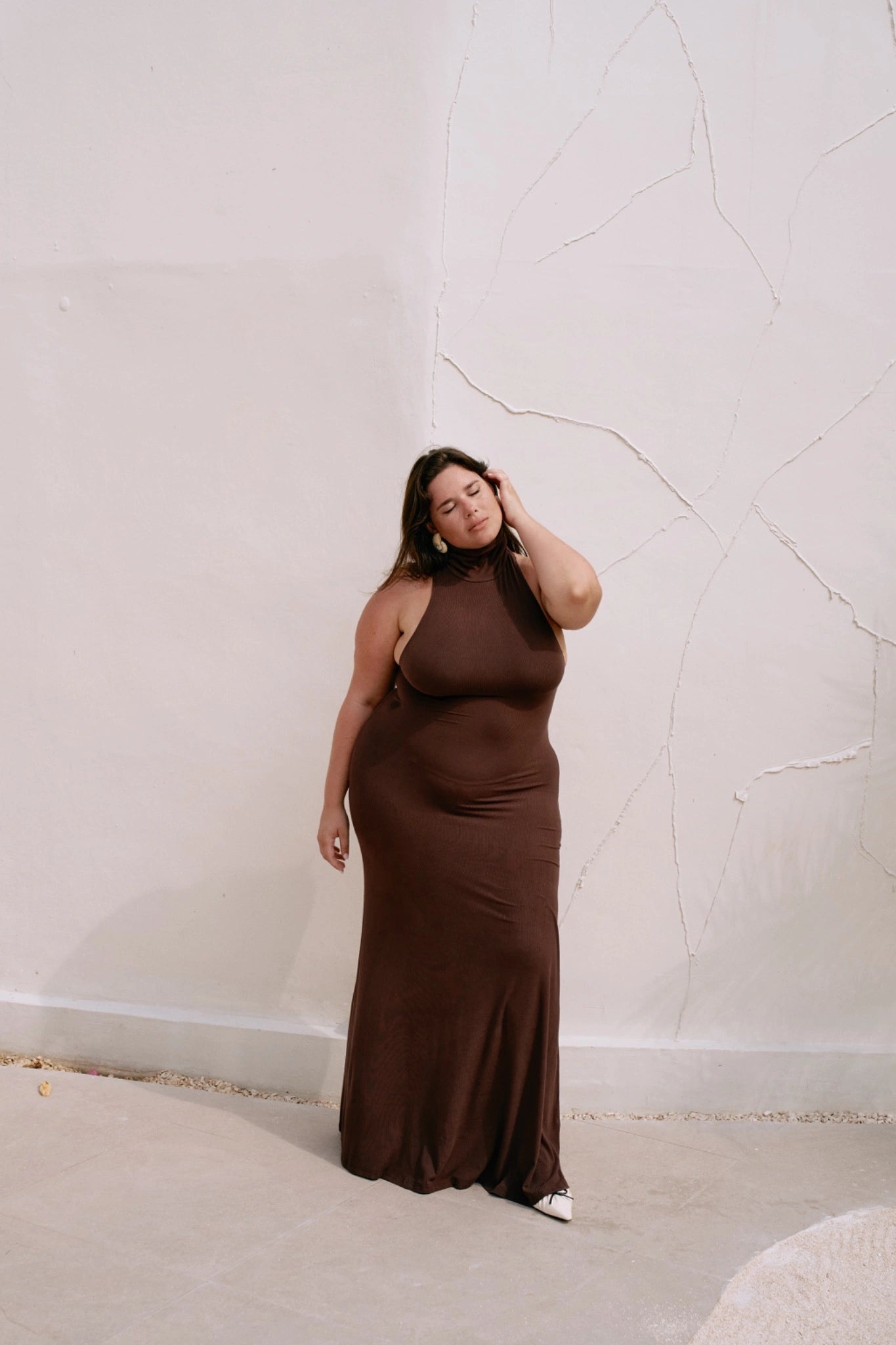 Woman wearing a brown dress against a neutral wall.