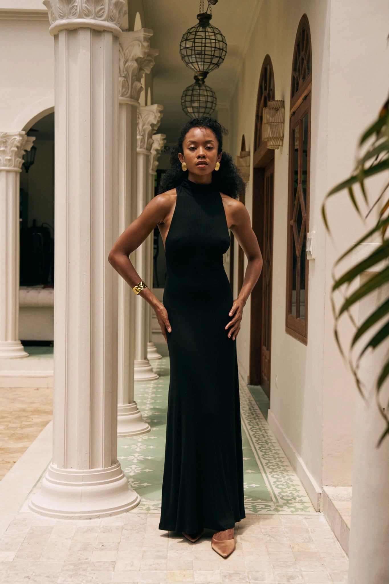 Woman in a black dress standing in an elegant hallway with columns and decorative lights.