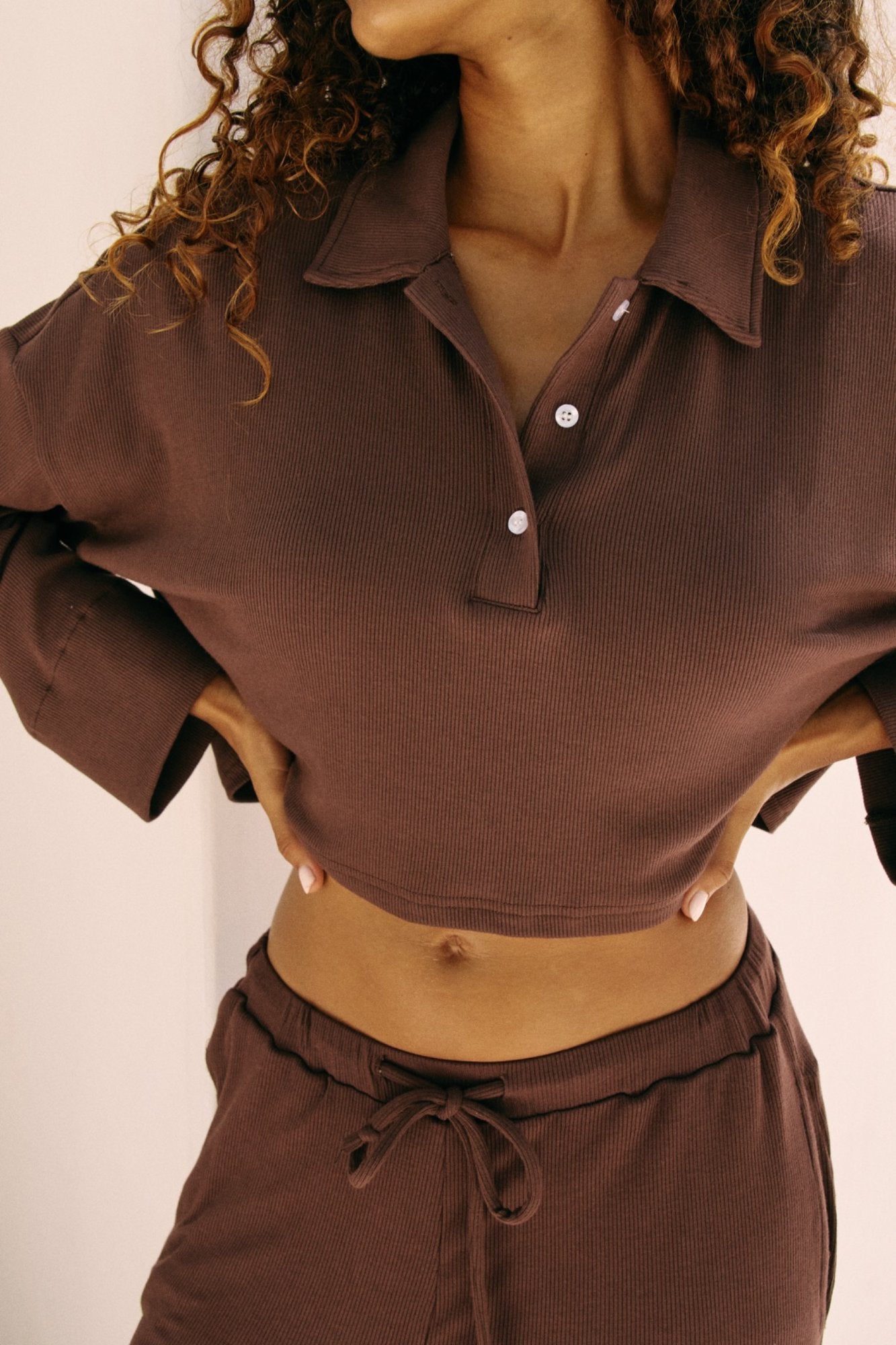 woman wearing a brown ribbed  long sleeved top and pants against a neutral background