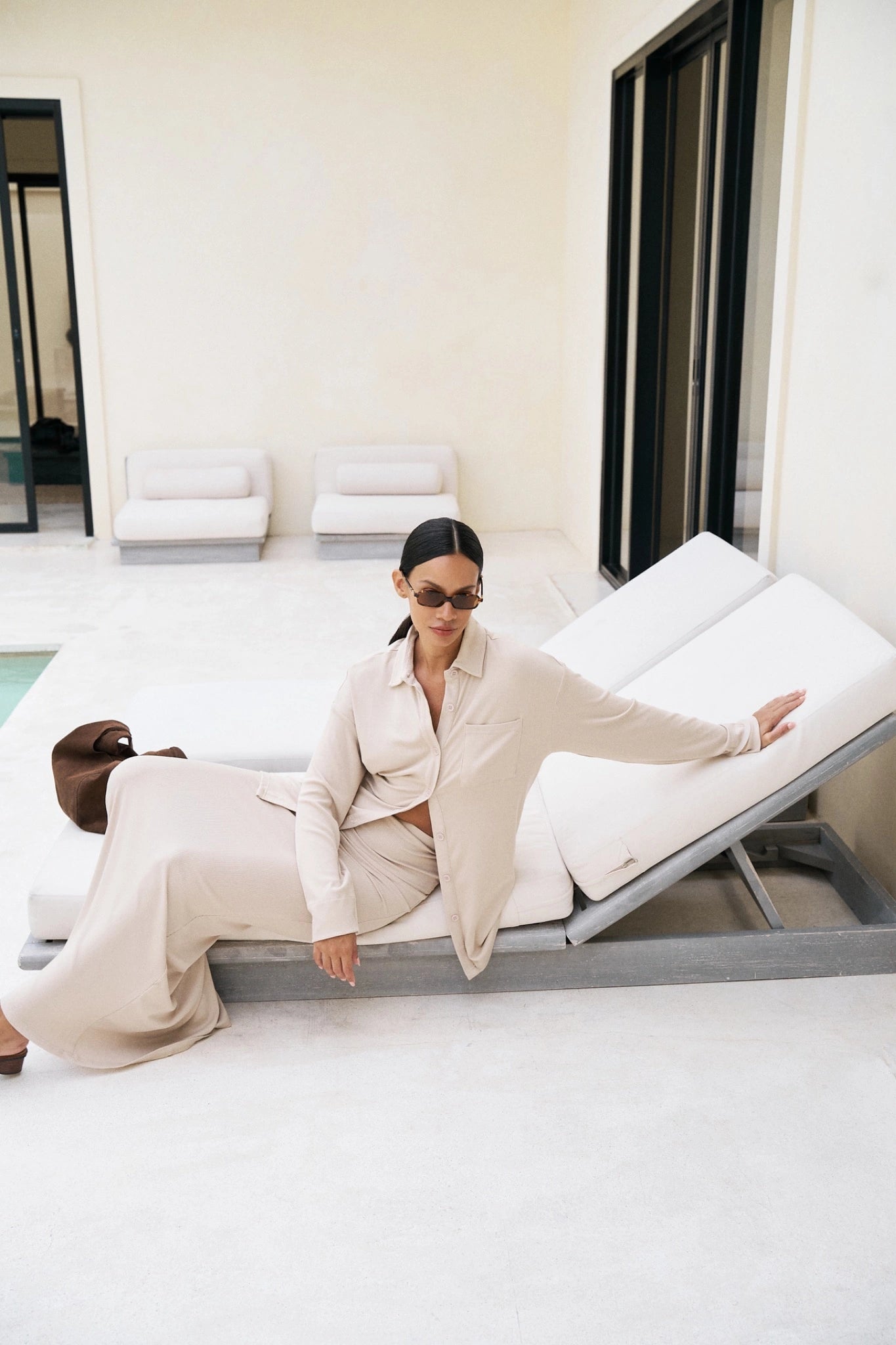 Woman in a beige outfit sitting on a modern white chair in a minimalistic room.