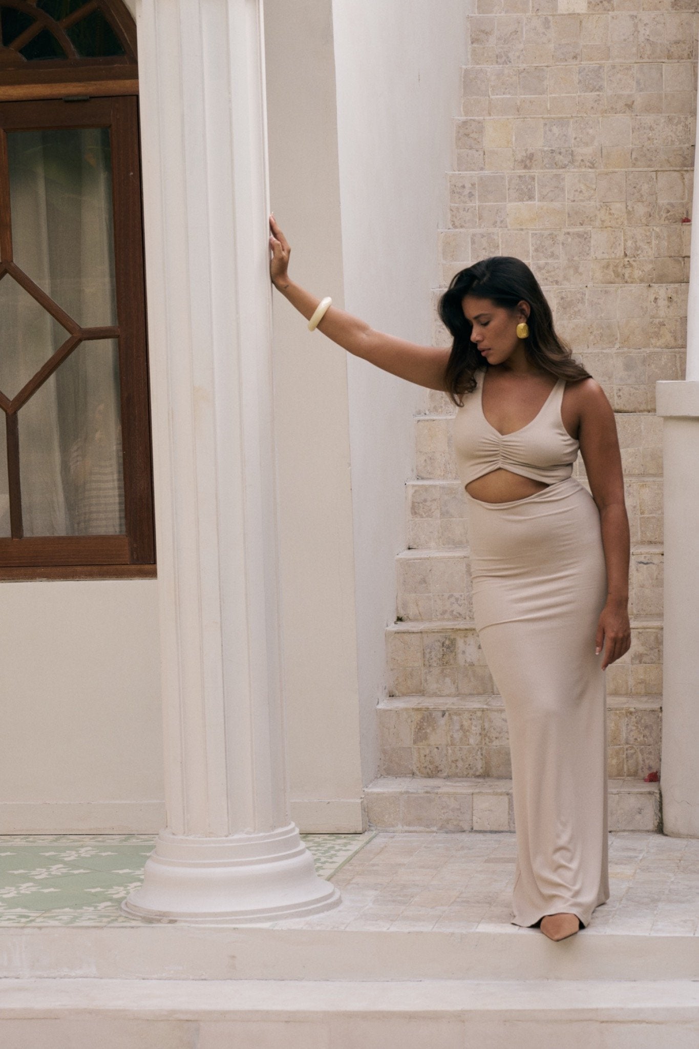 Model wearing the Reily cutout maxi dress in Coconut, standing by a white column